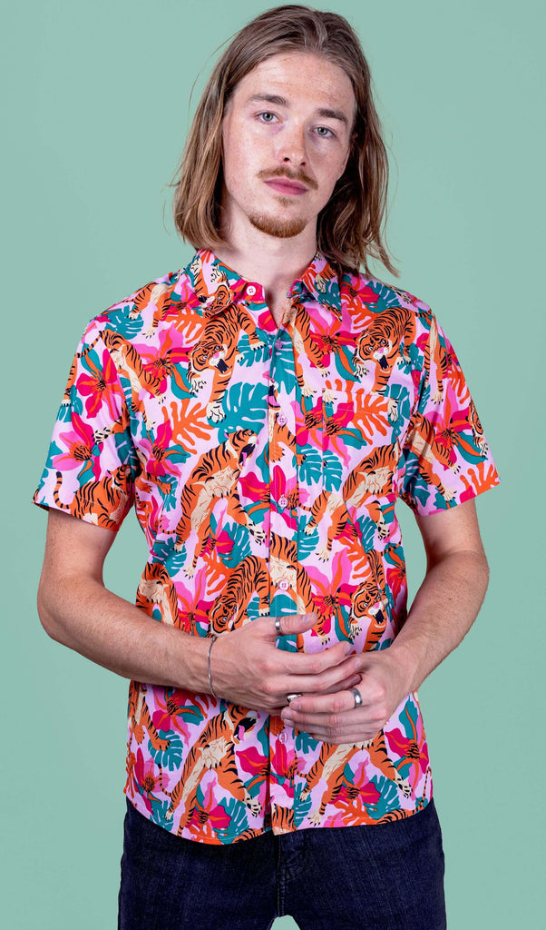 Jack is stood in a photography studio in Hove with a green backdrop wearing Tiger Lily Stretch Short Sleeve Shirt with jeans. The baby pink shirt has an all over print of tigers with flowers and leaves. Jack is posing toward the camera with his hands together.