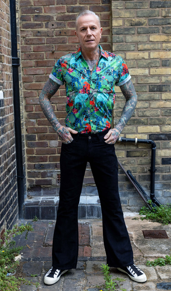 Jim is standing in a mews in Hove he is a tattooed grey haired man he is wearing a jungle print shirt and black flares by Run & Fly