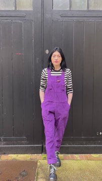 Gabrielle is wearing the purple magic stretch corduroy dungarees with black and white long sleeve top and chunky boots, model is posing in outfit and walking around. 