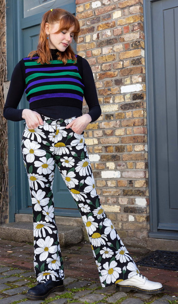 A ginger tall model with shoulder length hair wearing daisy print flares and a striped tank top with one black and one white boot shot in a mews in Hove