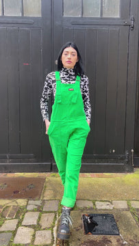Gabriella a tall black haired model is wearing a green pair of corduroy dungarees with a cow print polo neck on underneath. She is against a black garage door in a mews shot by Amy Davies Photography in Hove
