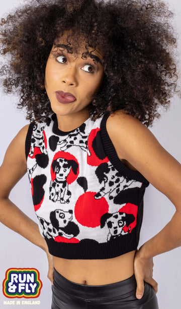 Cindy is stood in front of a white studio background wearing the seeing spots Dalmatian knitted tank top with leather look leggings. They are facing forward posing with both hands on their hips, sticking their tongue out and looking off to the right. Photo is cropped from the hips up.