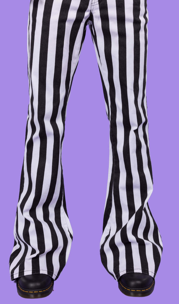 Close up of Richard wearing the Black & White Striped Bell Bottom Stretch Super Flares with black shoes. He is facing the camera in front of a lilac backdrop. The photo is cropped at the waist.