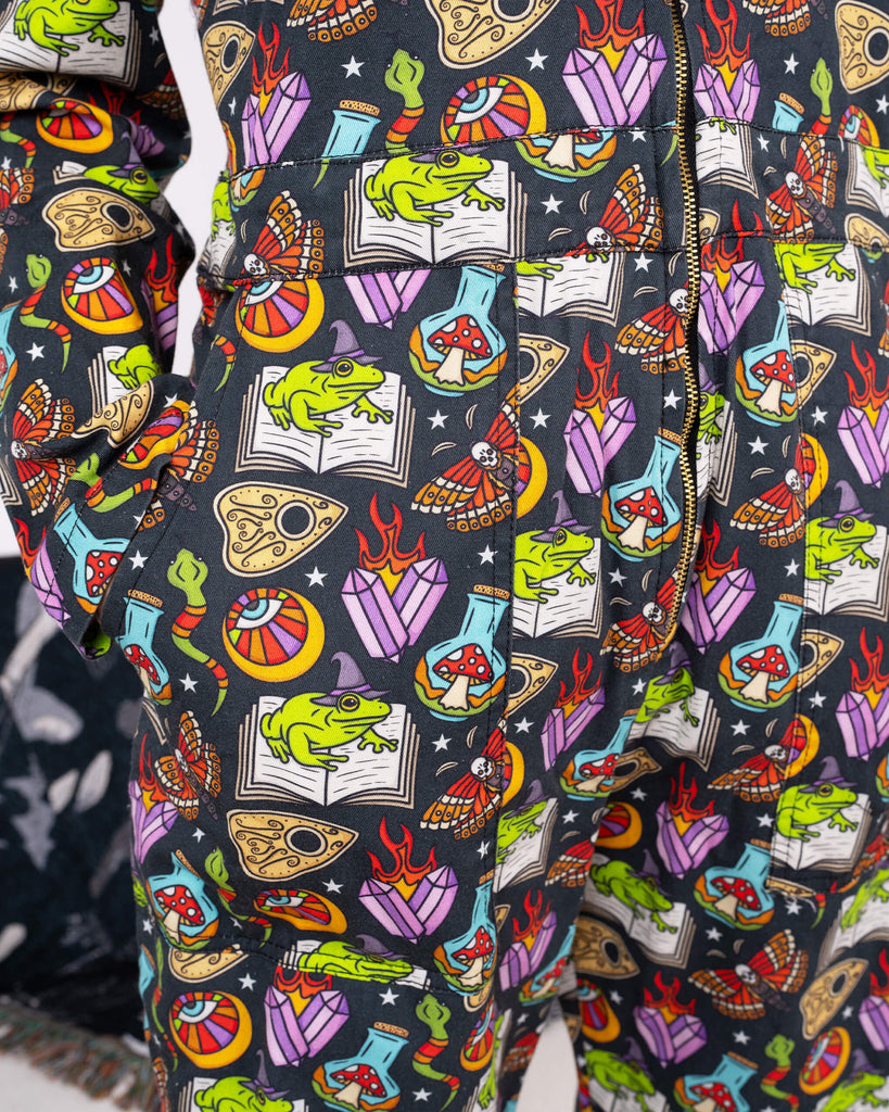 A detailed look at the Halloween: Bewitched Boiler Suit by Run & Fly. The fabric features whimsical illustrations of frogs, mushrooms, and mystical motifs, showcasing the brand’s quirky and ethical slow fashion ethos.