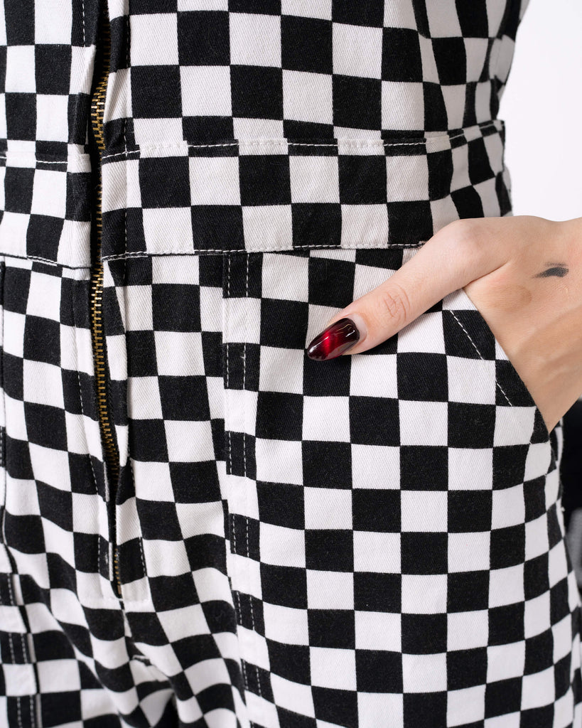 A detail shot of the Black & White Checkerboard Stretch Twill Boiler Suit by Run & Fly. The image highlights the gold zip front, functional side pockets, and bold checkerboard print. A sustainable and stylish slow fashion staple.