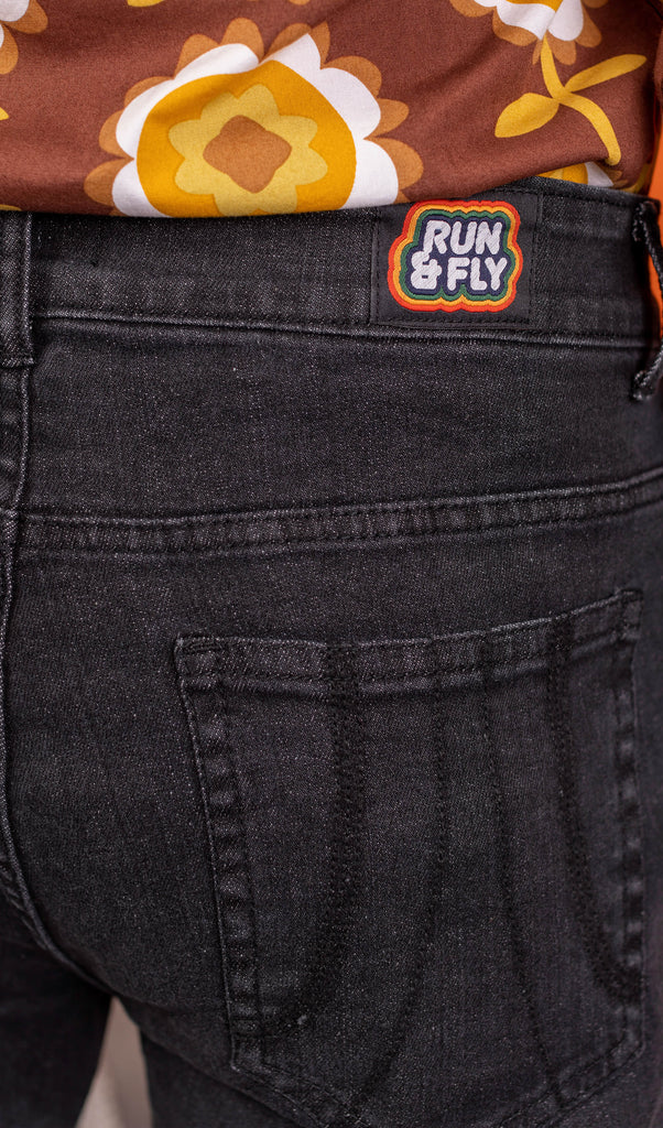 Close up of the back pocket stitching detail on the Black Stone Wash Regular Rise Bell Bottom Super Flares paired with the brown retro flowers long sleeve shirt modelled by Jack. You can also see the Run & Fly logo label on the back waistband. The denim jeans trousers are regular rise with a stonewashed lighter black colour, fitted to thigh and flared bottoms.