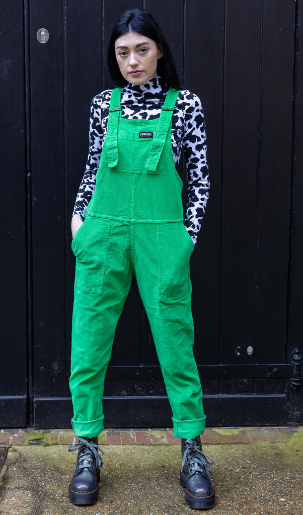 Gabriella a tall black haired model is wearing a green pair of corduroy dungarees with a cow print polo neck on underneath. She is against a black garage door in a mews shot by Amy Davies Photography in Hove