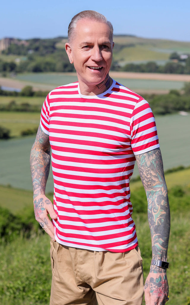 James is wearing the White & Red Stripe Short Sleeve T Shirt with tan coloured shorts, showing off his many tattoos in a grassy field
