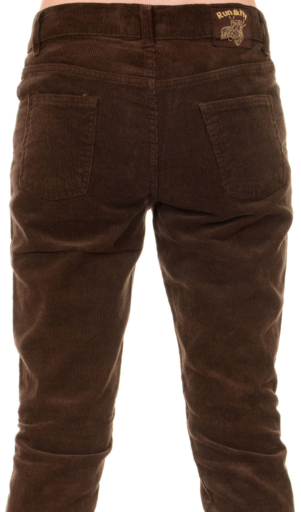 Model is stood in front of a white studio background wearing the mens 60s brown corduroy slim fit jeans with black trainers. They are facing away from the camera. Photo is a close up cropped from the waist down to the knees.