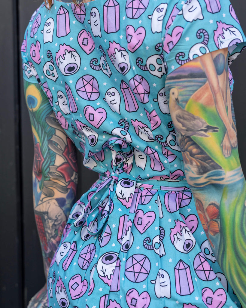 Close-up back view of a blue dress with a cute ghost and heart pattern, worn by a red-haired woman with detailed arm tattoos. The dress is designed by Run & Fly, a small ethical fashion brand focused on slow, sustainable fashion.