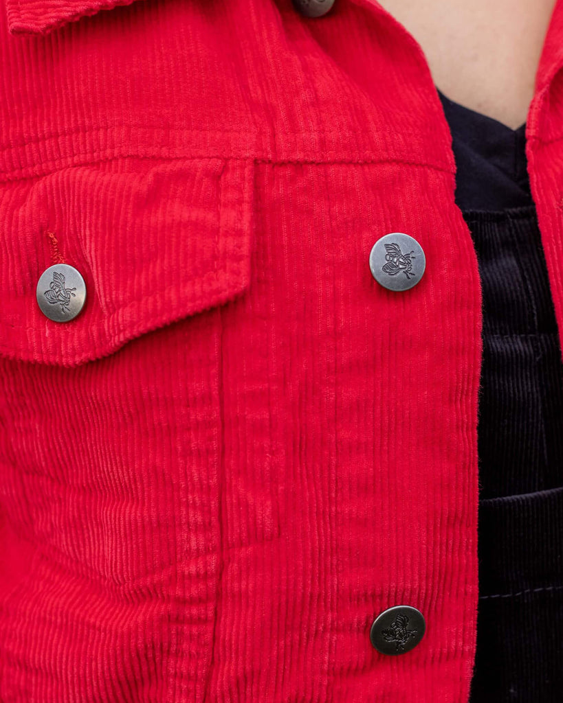 Close up shot of the front pocket detailing on the retro vintage red cord unisex western jacket over black dungarees.