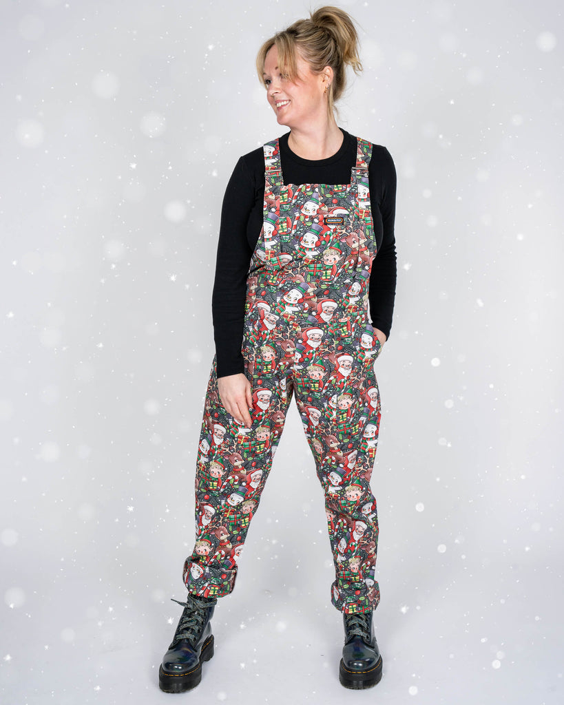 Karina poses confidently, showing off the cheerful holiday design of Run & Fly’s Christmas dungarees. The snowflake overlay gives the image a whimsical, seasonal vibe, perfect for celebrating the festive spirit.