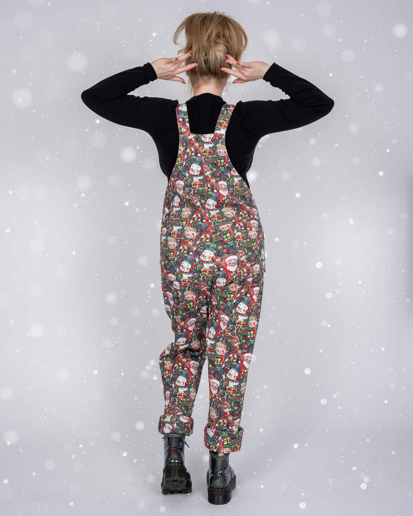 A back view of Karina modelling Run & Fly’s Christmas-themed dungarees. The retro holiday print features Santa, reindeer, and other festive motifs, all set against a snowy backdrop. Karina playfully adjusts her hair, revealing the relaxed fit of the dungarees.