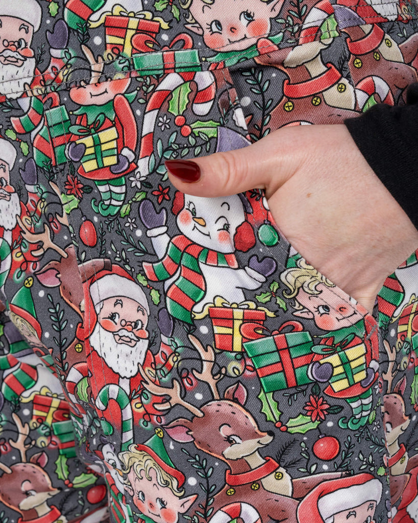 A close-up of a Run & Fly dungarees pocket, highlighting the intricate Christmas-themed details, including Santa, elves, and presents. Karina’s hand rests in the pocket, showcasing the functional and stylish design.