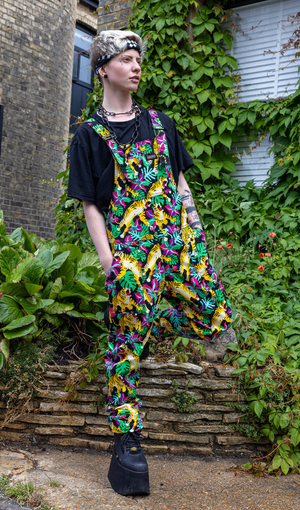 Jamie a masc trans model with blonde short hair and black tattoos wearing black dungarees with yellow tigers and a matching black tee and chains underneath shot in Hove by Amy Davies Photography