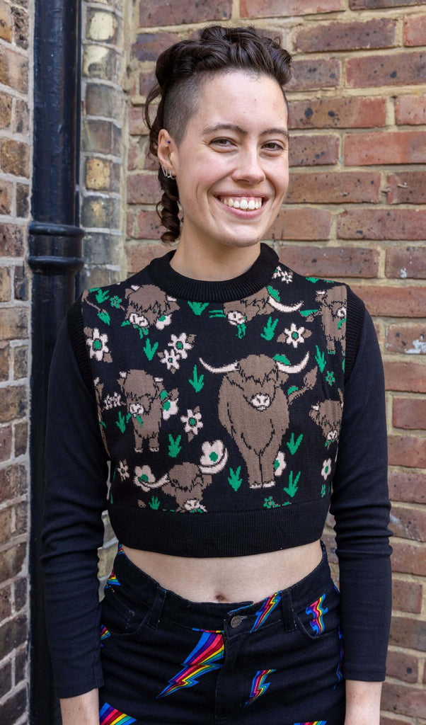 model with shaved sides of their hair smiling at camera wearing a cropped tank top with knitted highland cows on