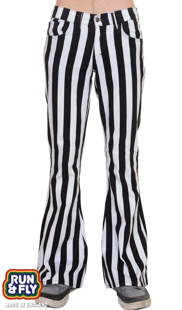 Model is facing the camera wearing black and white vertically striped bell bottom flares with grey and black trainers. Photo is cropped from the waist down.