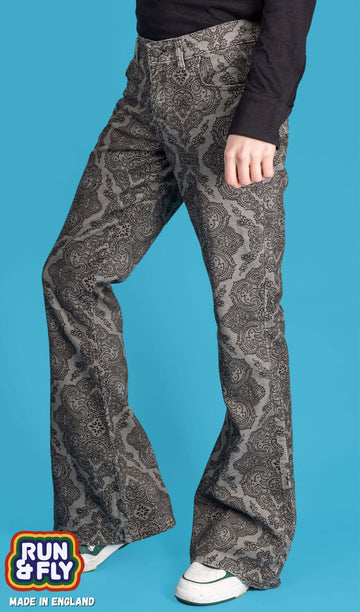Jack is stood in front of a blue studio background wearing the silver Hendrix paisley with a long sleeve black shirt and white trainers. They are facing to the left with one leg bent forward highlighting the flare shape. Photo is cropped from the waist down.