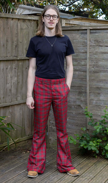 Jack is stood outside in front of a wooden fence wearing Retro Red Royal Stewart Tartan Plaid Bell Bottom Trousers with a black short sleeve t shirt and brown shoes. He is facing the camera and posing with one hand in the pocket of the trousers.