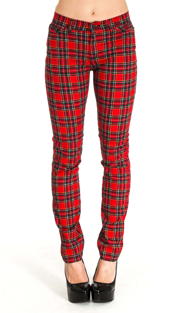 Model is stood in front of a white studio background wearing the mid rise red tartan stretch skinny jeans with black heels. They are facing forward with both feet placed together. Photo is cropped from the waist down.