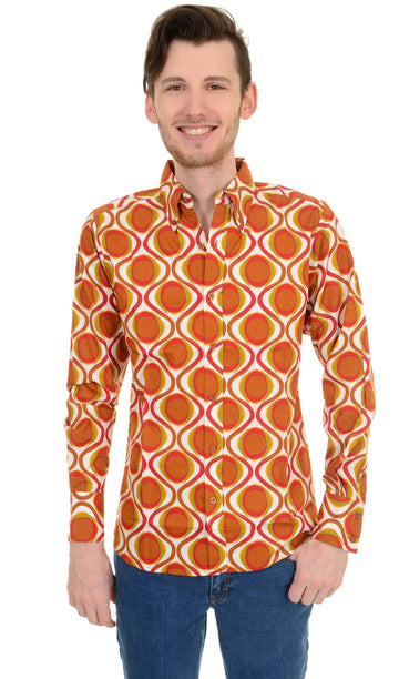 Model is stood in front of a white studio background wearing the retro mod geometric psychedelic printed 70s shirt with blue jeans. They are facing forward with both arms resting by their side whilst smiling. Photo is cropped from the hips up.