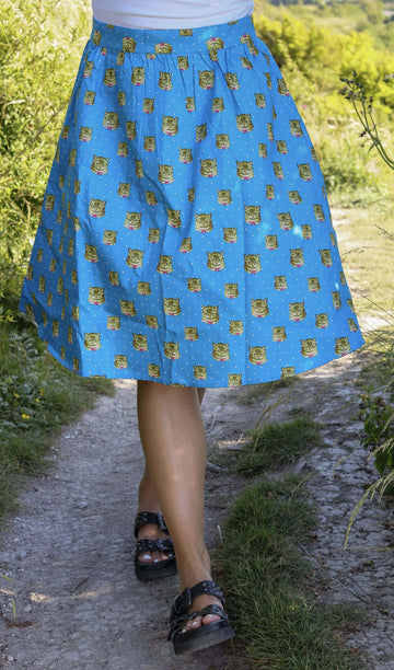 Model is walking through a grassy area wearing the kitty cat retro a line skirt with a white tshirt and black sandals. Photo is cropped from the waist down.