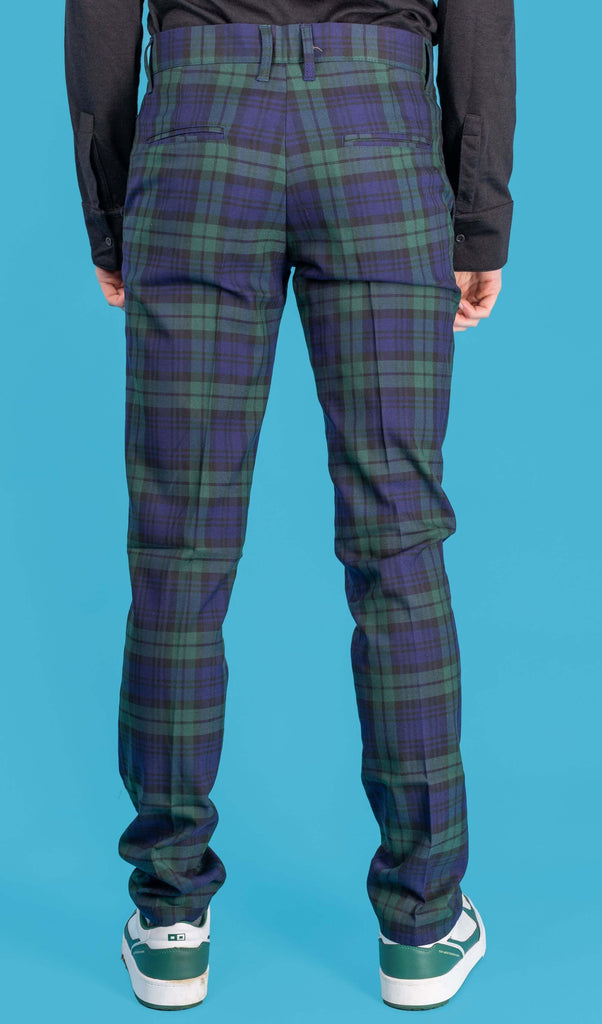 Jack is stood in front of a blue studio background wearing the retro mod stretch black watch tartan trousers with a long sleeve black tshirt and white trainers. They are facing away from the camera with both arms resting by their side. Photo is cropped from the waist down.