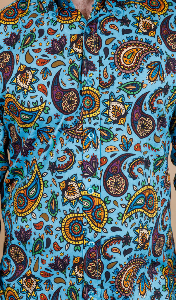 close up of Sky Blue Paisley Print Long Sleeve Shirt. The shirt is a sky blue colour with an all over paisley print in various muted rainbow colours.