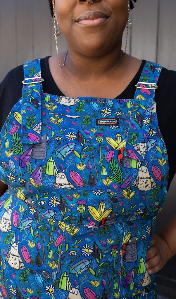 close up of Han wearing Run & Fly x Katie Abey Crystal Critters Stretch Twill Long Pinafore Dress with rainbow Run&Fly logo on the front bib of the dungarees.