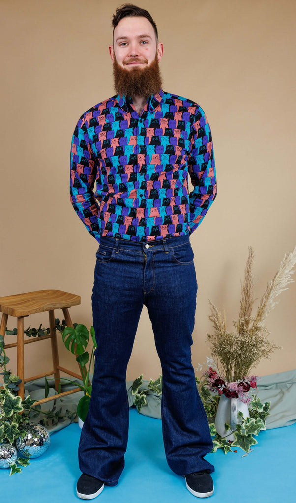 male model wearing Indigo Blue Mid-Low Rise Bell Bottom Super Flare paired with Cat Chorus Print Long Sleeve Shirt. He is stood in a studio in Hove smiling toward the camera with his hands behind his back. 