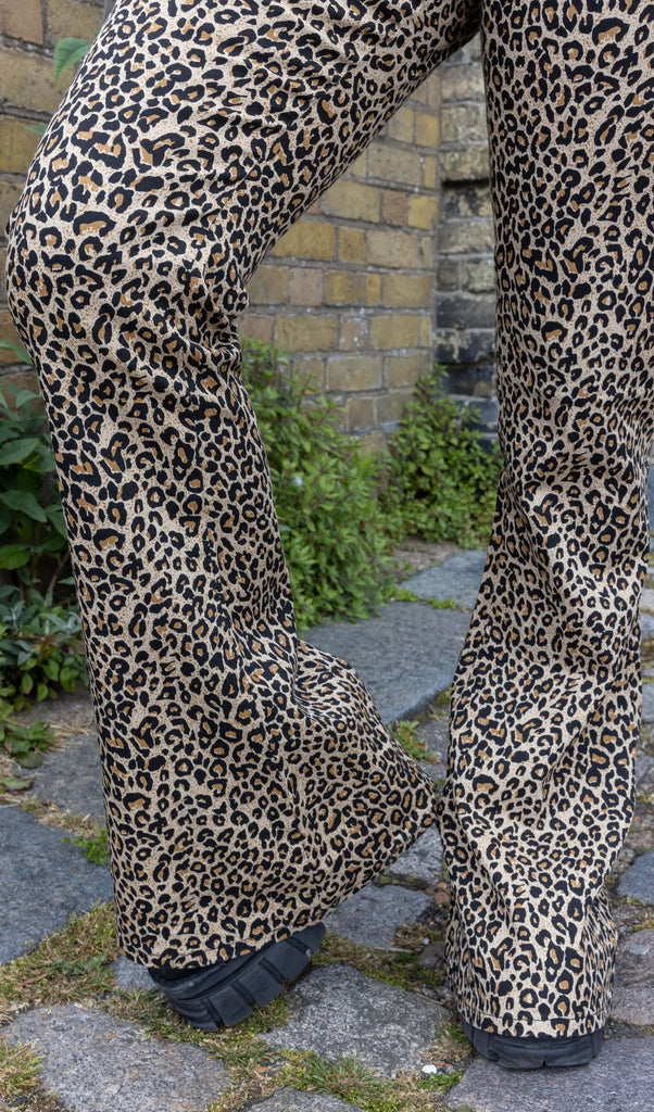 Close up of model wearing Leopard Print Bell Bottom Stretch Super Flares, paired with chunky black boots. The flares are a natural leopard print pattern. Close up shows the flared bottoms covering model's boots.