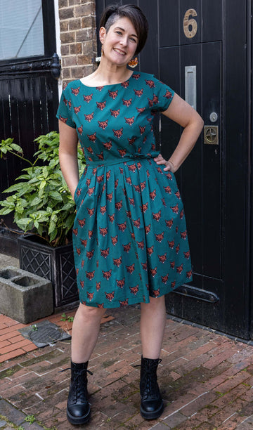 Sarah is stood by a black door outside in Hove wearing Stretch Foxy Print Tea Party Dress with Pockets with black boots. The emerald green dress has an all over fox head print. Sarah is smiling at the camera with one hand on her hip and other in the dress pocket. 