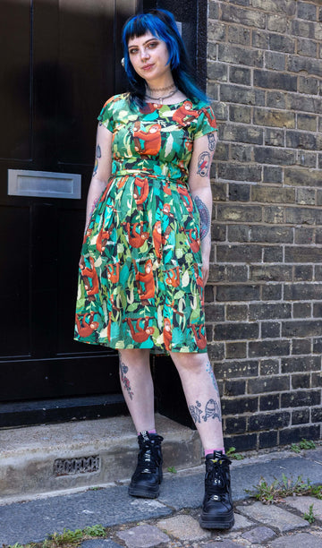 Faeryn is stood outside in Hove in a mews wearing Orangutan Stretch Belted Tea Dress with Pockets paired with black boots. The green dress has an all over orangutan print with leaves and branches. Faeryn is posing facing the camera. 