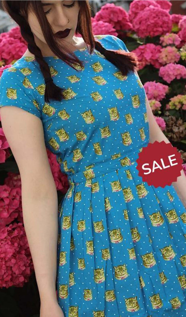 Alice is stood in front of a floral background wearing the kitsch kitty polka dot tea party dress. She is looking down to the left. Photo is cropped from the hips up.