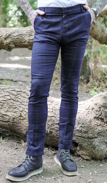 Jim is stood in a forest area wearing the retro mod stretch navy plaid tartan slim skinny fitting trousers with a white short sleeve tshirt and brown boat shoes. They are facing forward with both hands in the side trouser pockets. Photo is cropped from the waist down.