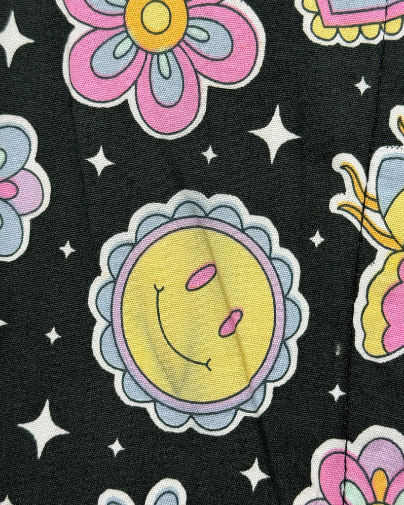A close-up of a printing issue on Run & Fly’s Bee Happy Stretch Jumpsuit. The yellow smiley sun is visibly faded in areas, with a greyish tint affecting the consistency of the design.