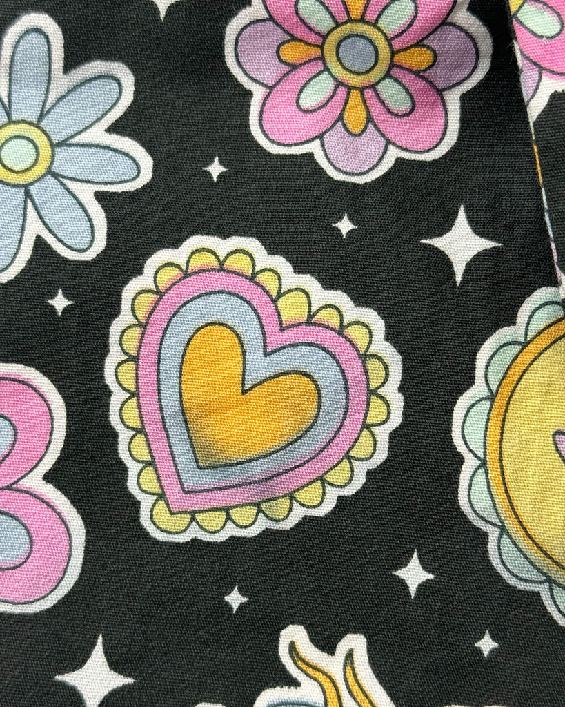 A fabric detail from the Bee Happy Stretch Jumpsuit by Run & Fly, showing a misprint. The yellow heart motif has a greyish patch, making the design appear faded and uneven.