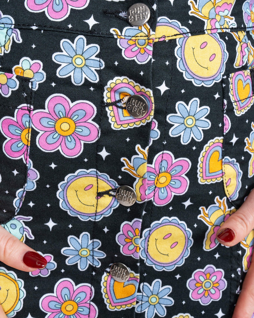 Detail shot of the Bee Happy skirt by Run & Fly. The joyful print by Waffle Mama Design includes smiley faces, flowers, hearts, and bees, accented with Run & Fly branded button fastenings.