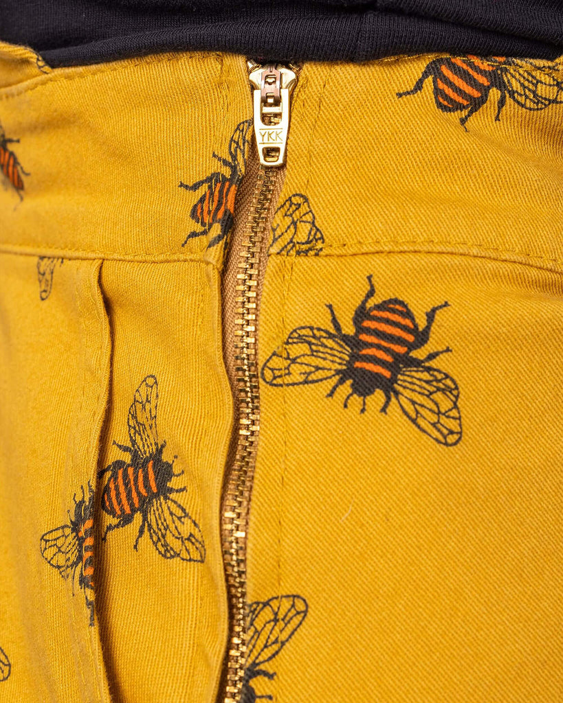 Close up shot of the bees knees bee print gold stretch twill pinafore dress zip up side.