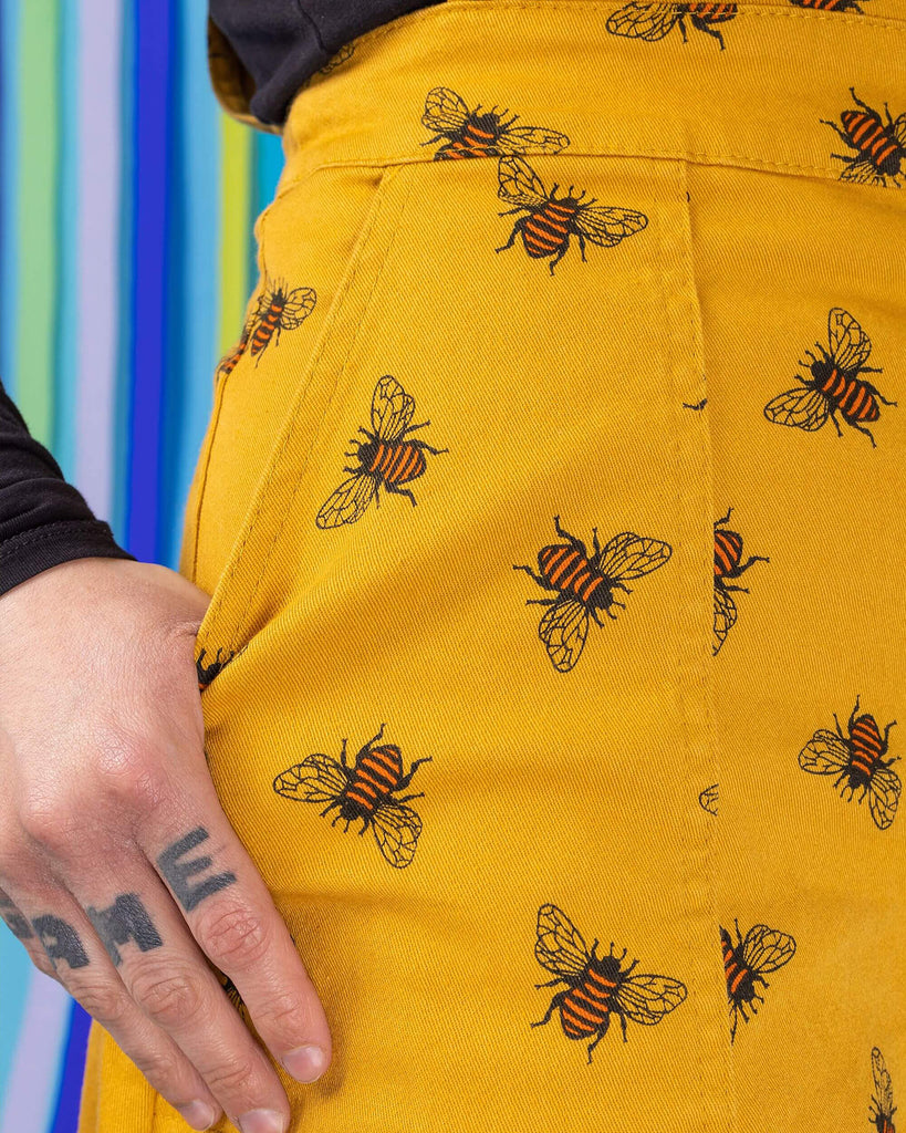 Close up shot of jojo's hand resting on the bees knees bee print gold stretch twill pinafore dress pocket.
