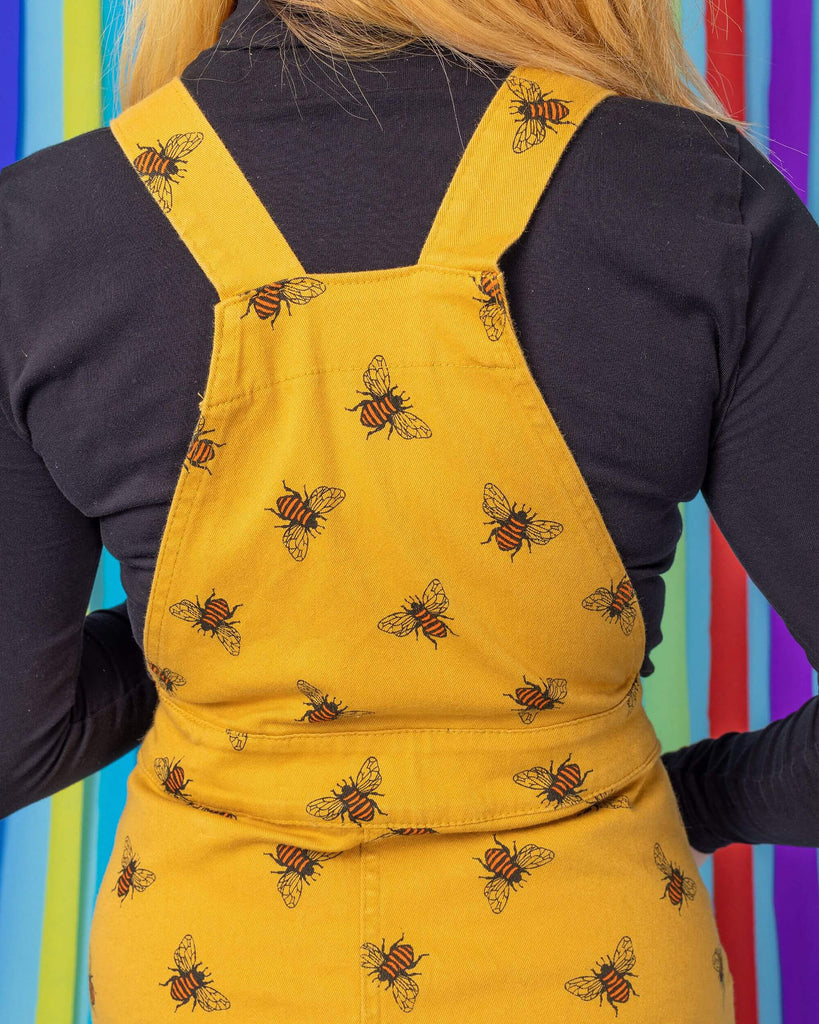 Close up shot of the back straps and back middle of the bees knees bee print gold stretch twill pinafore dress modelled on jojo.