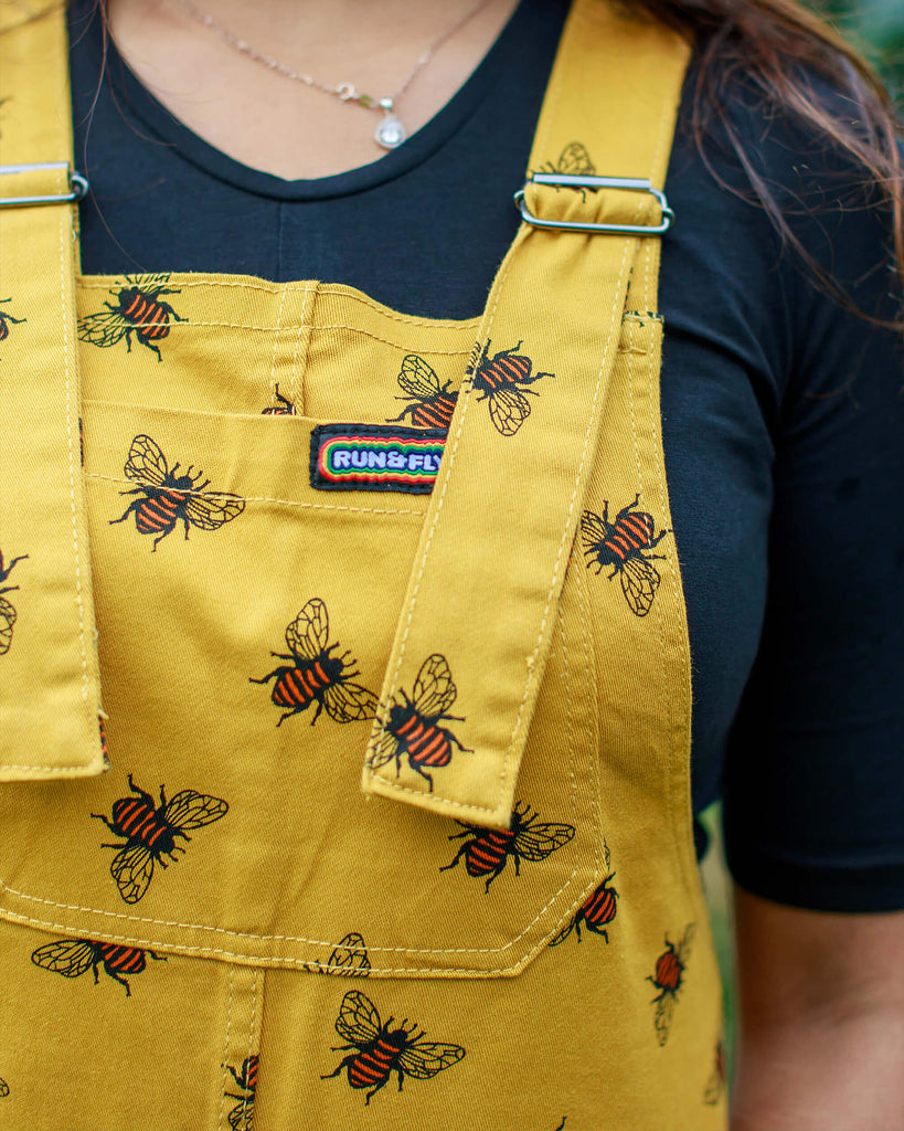 Close up photo of Jarin wearing the Bees Knees Gold Stretch Twill Dungarees with a black tee and her hair is falling over her shoulders.