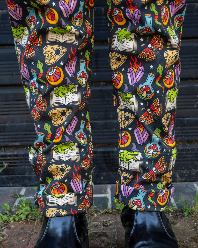 Close-up shot of the lower half of a person wearing Run & Fly dungarees, highlighting the whimsical print that includes frogs, moths, and mystical symbols. The person is also wearing chunky black boots, adding to the alternative fashion style.