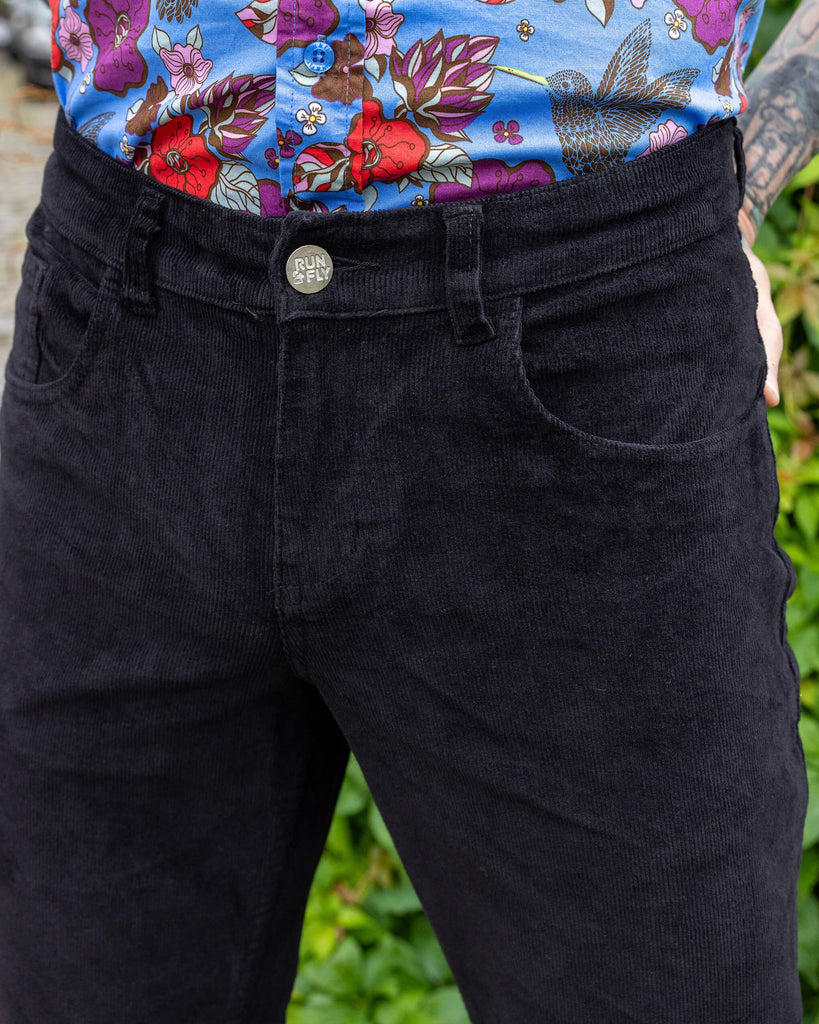 Close up of model wearing Black Corduroy Bell Bottom Flares. The close up shows belt loops, pockets and silver button on the flares with Run&Fly logo.
