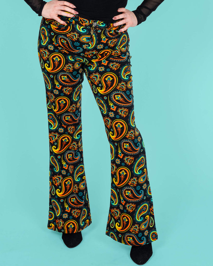 Half length front view of Run & Fly's black paisley flares, styled with a fitted black top. The bold orange, turquoise, and yellow paisley print and retro flared silhouette create a vintage-inspired, ethical slow fashion statement.
