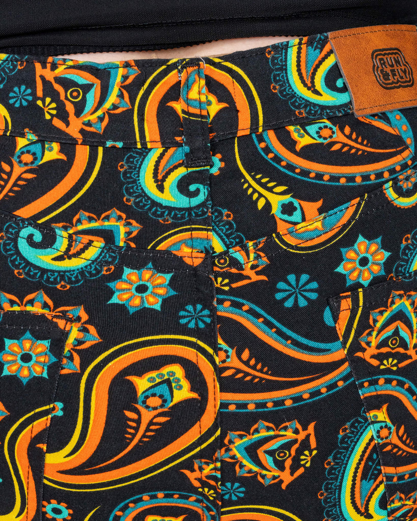 A close-up of the back of the black paisley flares by Run & Fly, showing the intricate retro paisley print and branded patch. The ethically crafted design highlights vibrant orange, yellow, and turquoise patterns.