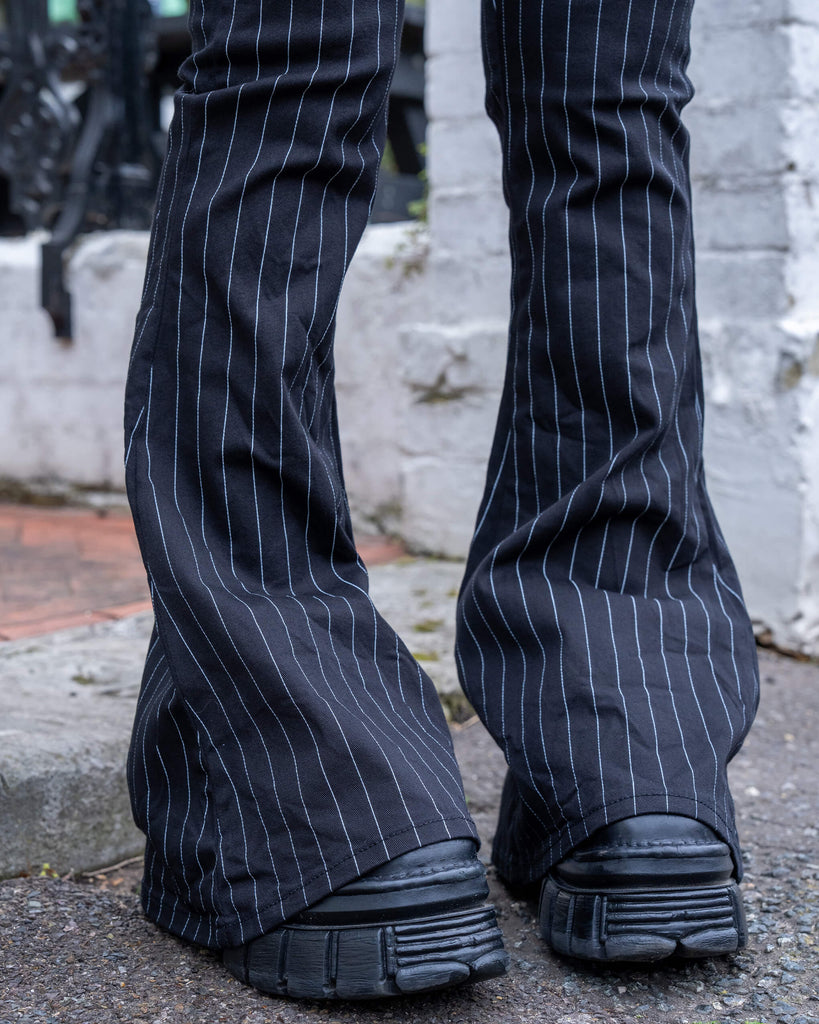 Hem-level close-up of the Run & Fly Pinstripe Bell Bottom Flares, showing the flared leg silhouette over chunky black shoes and the sharp vertical white stripe detail.