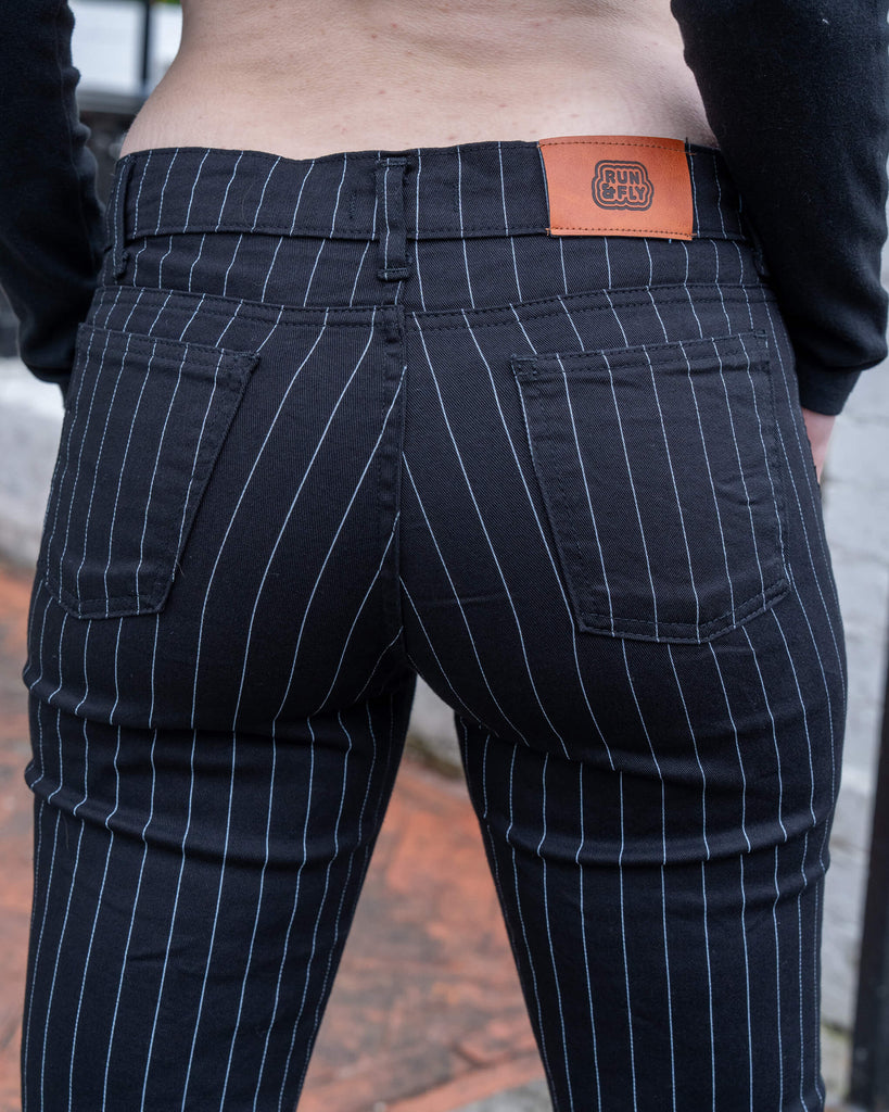 Close-up of the back waistband and pockets on the Run & Fly Black & White Pinstripe Flares, showing vertical white pinstripes, detailed stitching, and a brown faux leather logo patch.