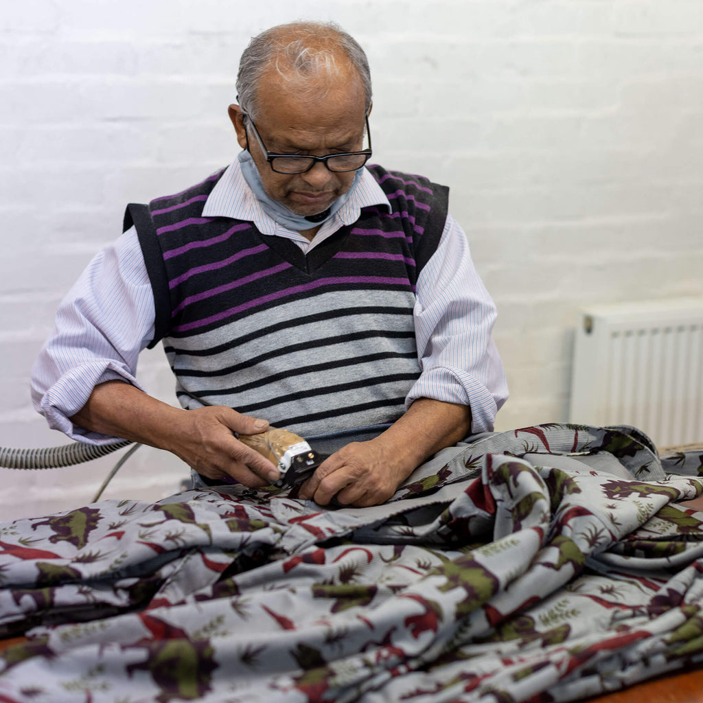 factory worker getting rid of spare threads on a pair of dinosaur dungarees