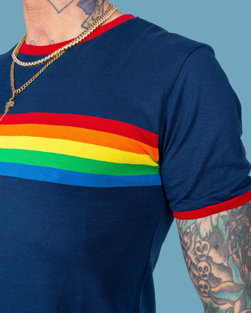 Close-up image of James modelling a navy t-shirt with a vibrant rainbow stripe across the chest. The details of the red trim on the neckline and sleeves add a bold contrast, complementing the colourful design.